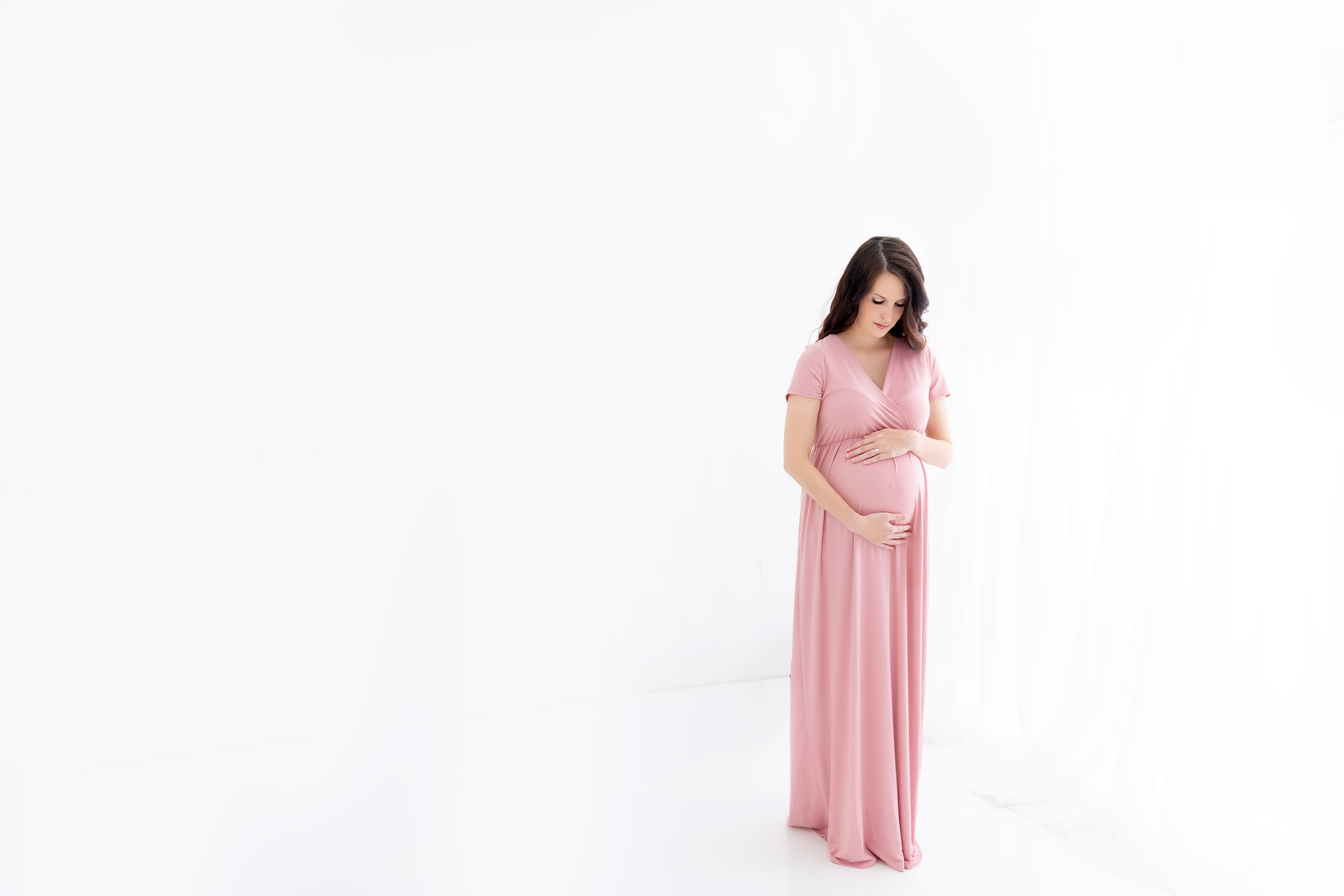 mom to be in a pink maternity gown standing in a studio after an appointment with a Midwife in Columbus GA